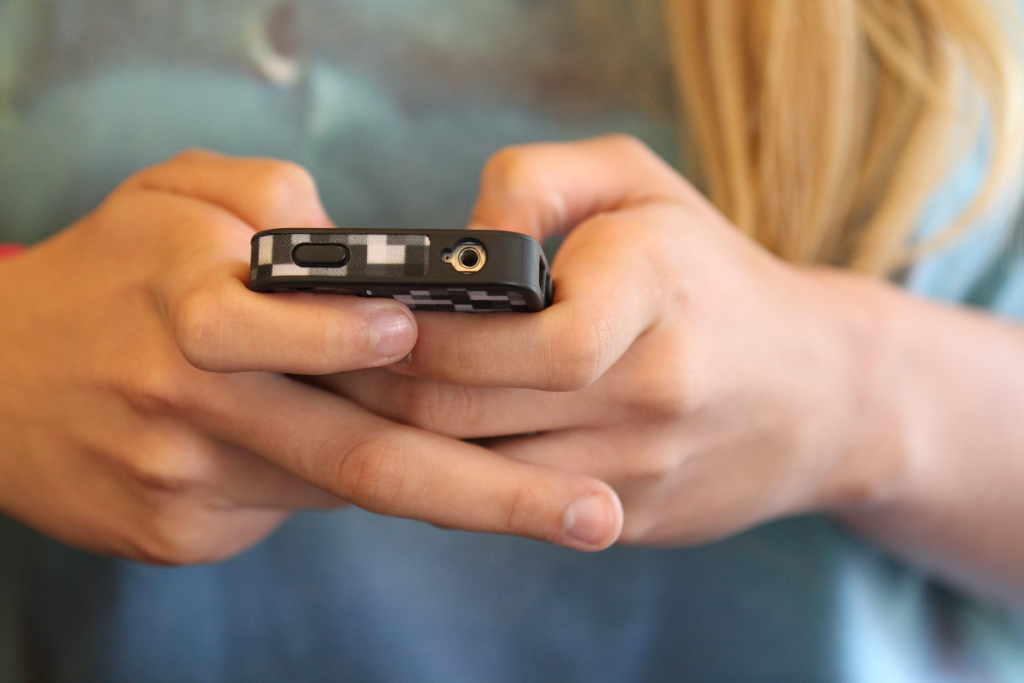 girl with long blonde hair texting on an iPhone 4 in a blue tank top